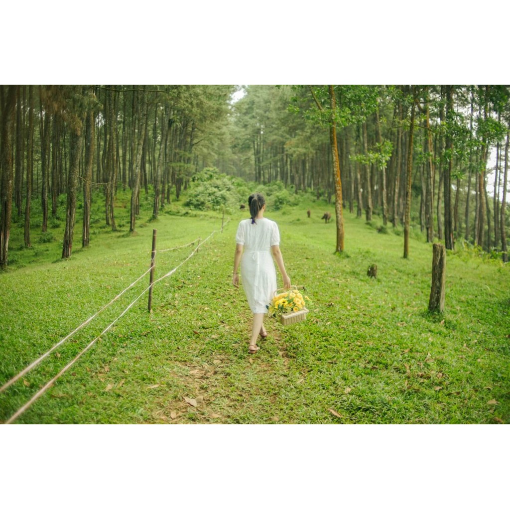 a woman in a white dress walking through a forest