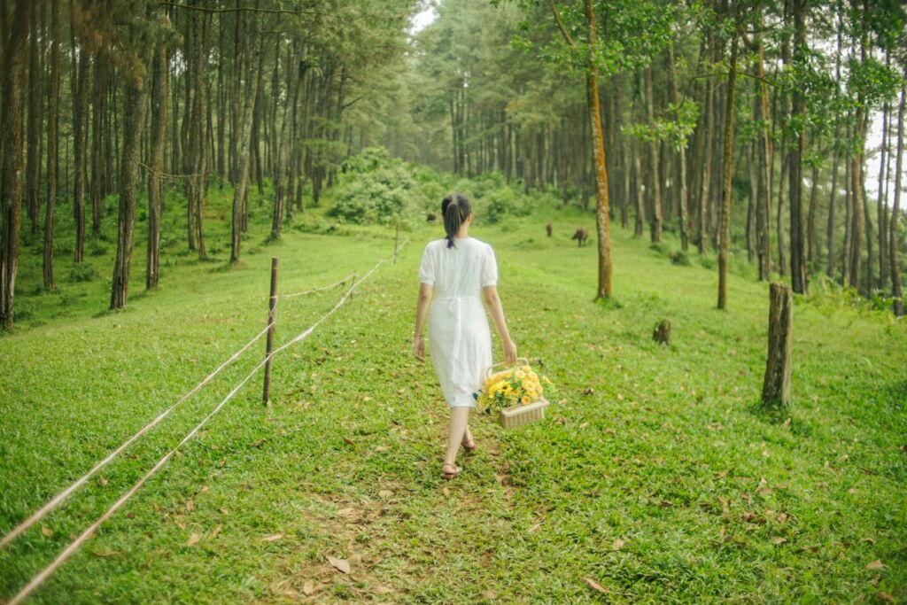 a woman in a white dress walking through a forest