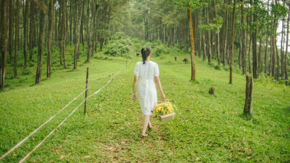 a woman in a white dress walking through a forest