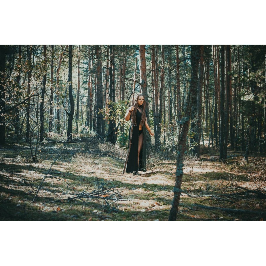 woman wearing black robe holding stick in the forest