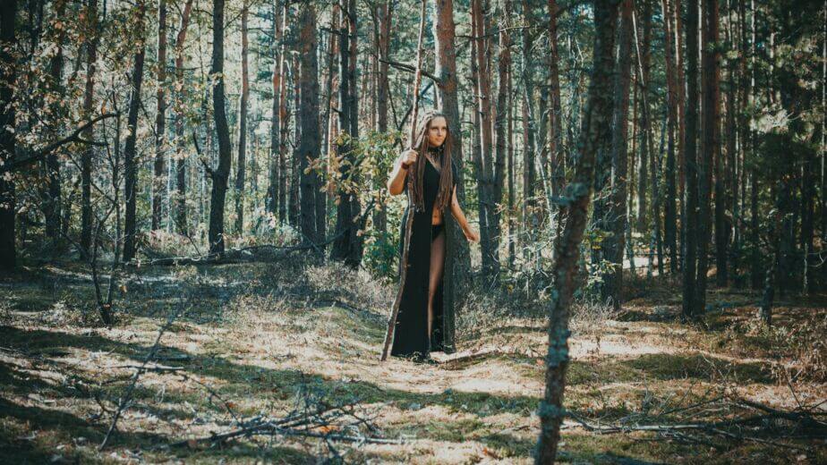 woman wearing black robe holding stick in the forest